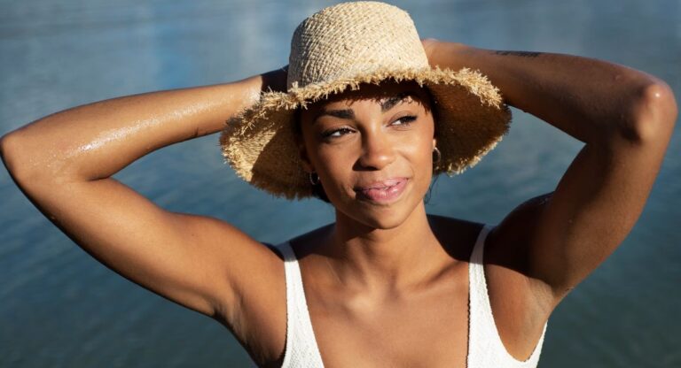 Black Woman in straw sun hat and white top - affordable sun protection clothing women choose for warm weather beach days