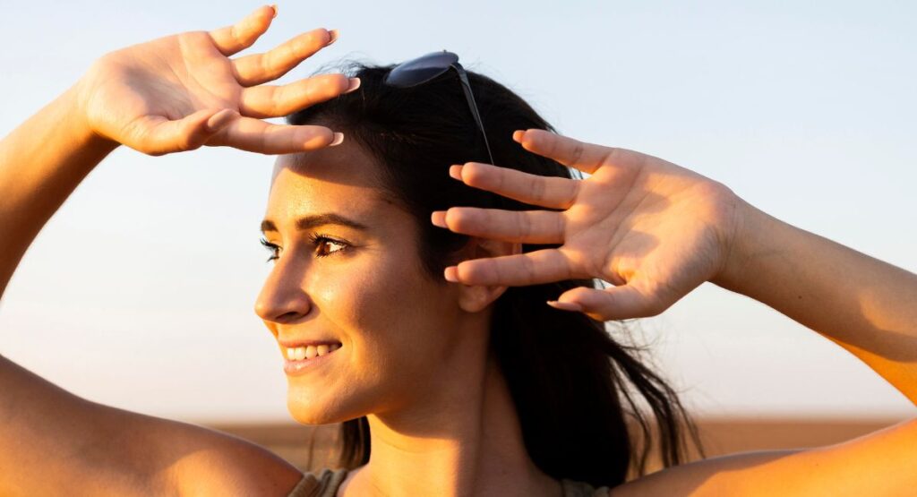 Dark-haired woman shielding her face from bright sunlight, showing proper sun safety practices with Sunbetter sunscreen