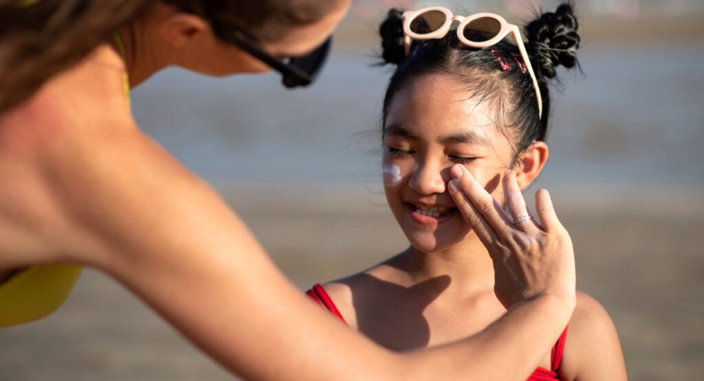 Parent applying Heliocare 360 Pediatrics Mineral Sunscreen SPF50 50ml to child's face at the beach
