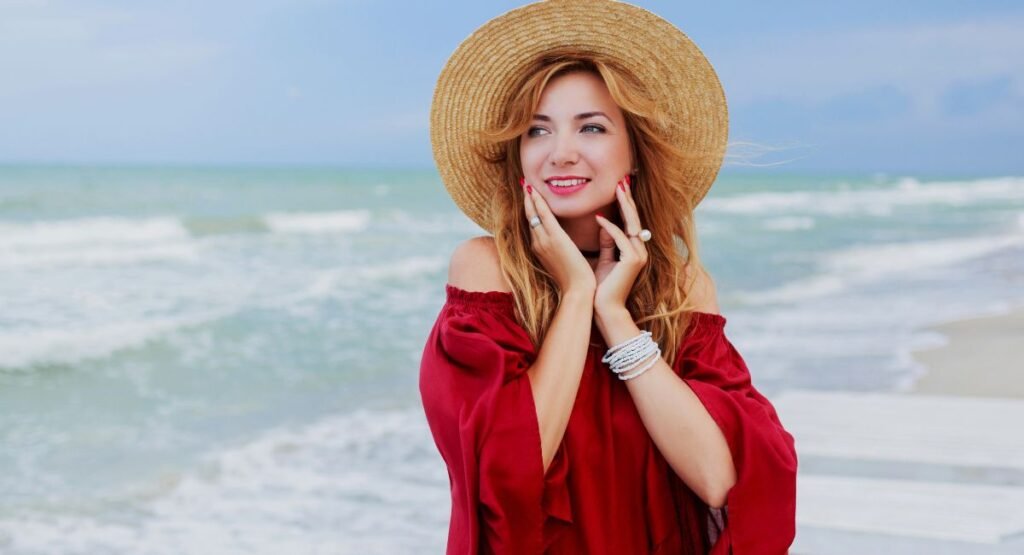 Smiling woman with red hair wearing straw hat at beach protected by Sunbetter sunscreen against ocean waves