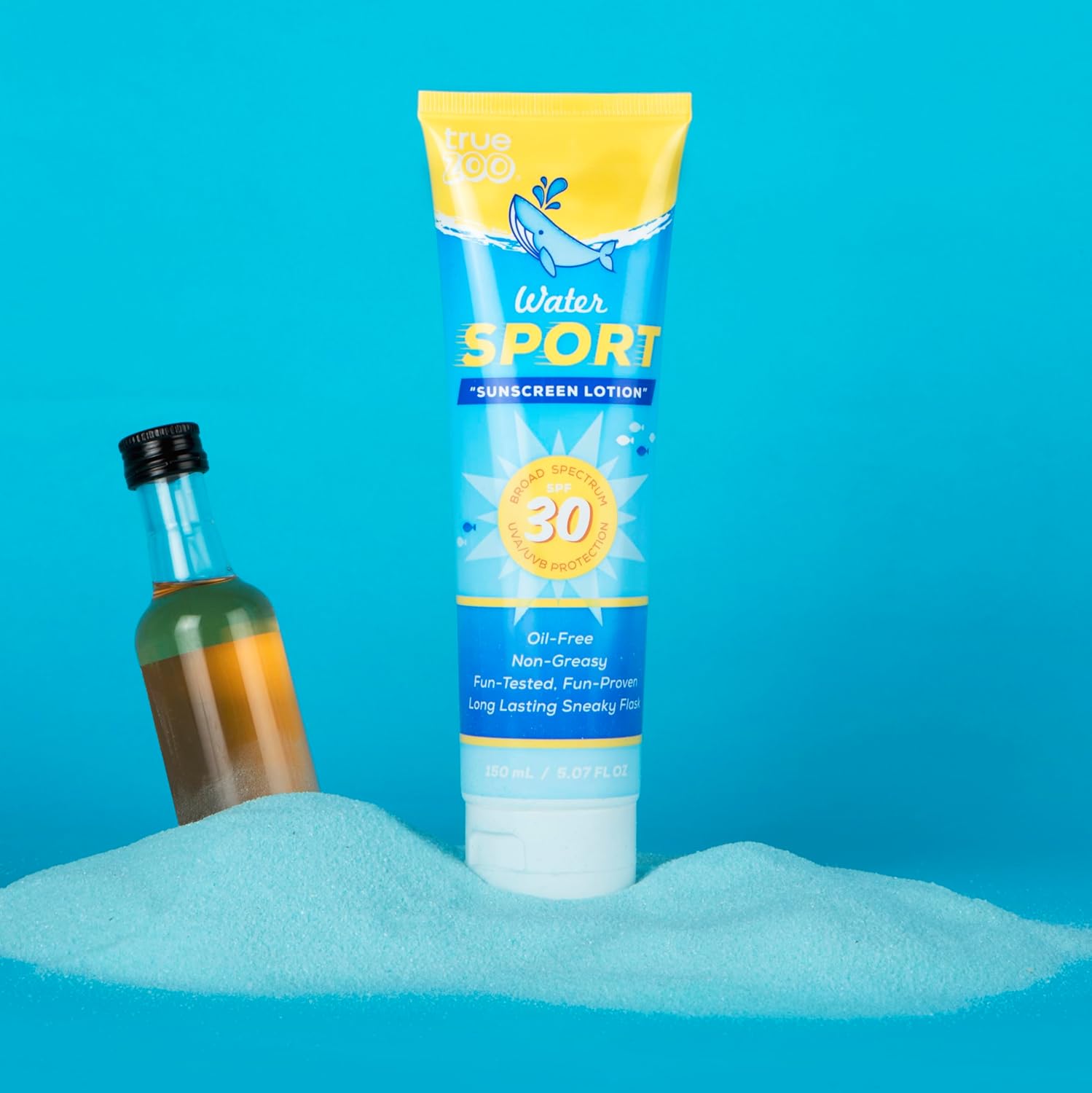 TrueZoo sunscreen lotion flask displayed on beach sand next to small alcohol bottle, showcasing its convincing disguise