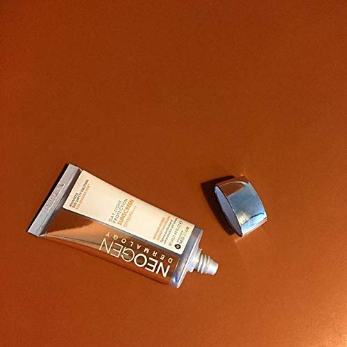 Neogen sunscreen tube with silver cap lying on terracotta orange surface showing SPF50 sun protection formula.