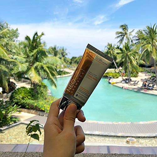 Person holding Neogen sunscreen tube at tropical resort with palm trees and swimming pool, showcasing vacation sun protection.