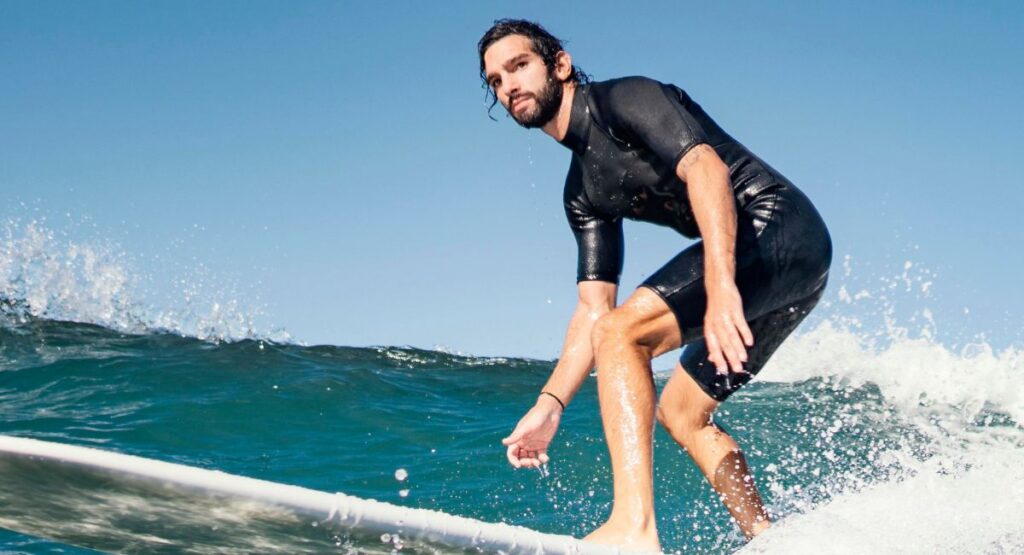 Surfer riding wave in fitted black neoprene wetsuit that provides UV protection while surfing - stylish sun protection clothing swimwear designed for active water sports with full upper body coverage against harmful sun exposure.